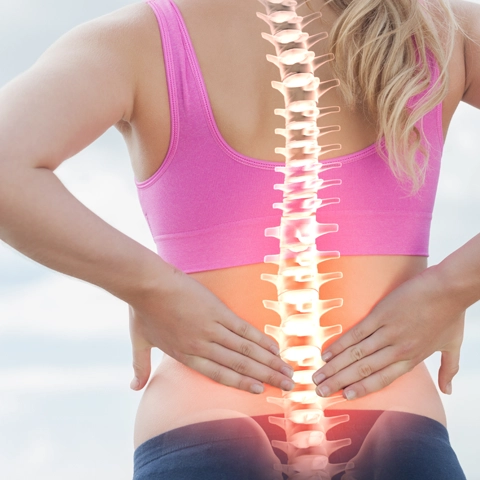 A woman holding her lower back. Her spine is highlighted red.