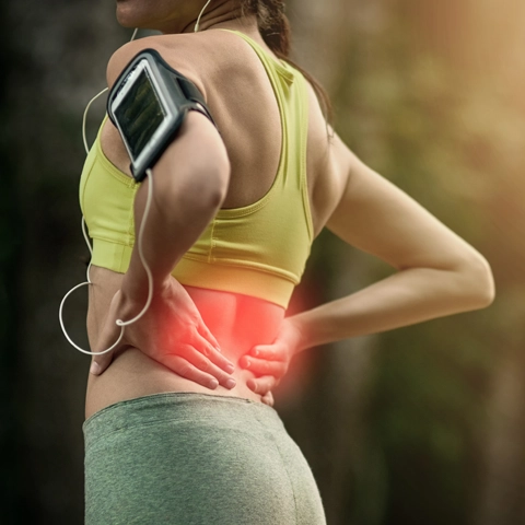 A woman in running clothes, holding her lower back that is highlighted red.