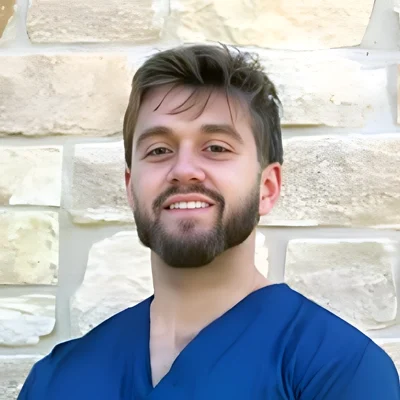 Dr. Matthew Grenda smiling in front of a stone wall.